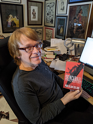 Max Allan Collins holding up a trade paperback of Reincarnal & Other Dark Tales