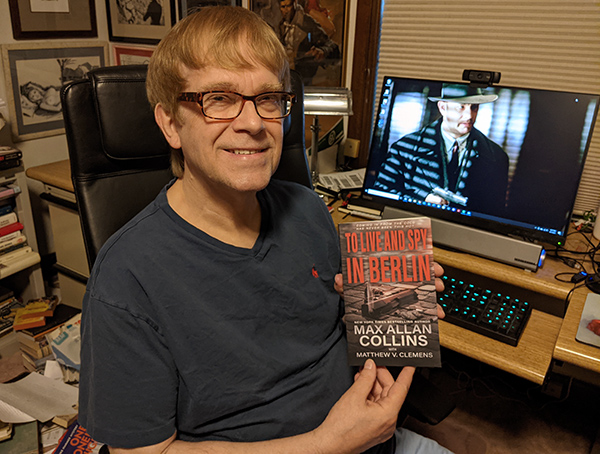 M.A.C. holding a copy of To Live and Spy in Berlin at his desk